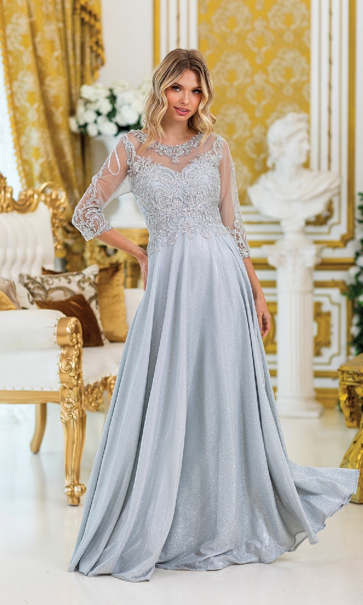 A woman in the Dancing Queen 4498 lace-sleeve long formal dress stands in an ornate gold and white room with classical accents, her elegant light gray gown beautifully embellished.